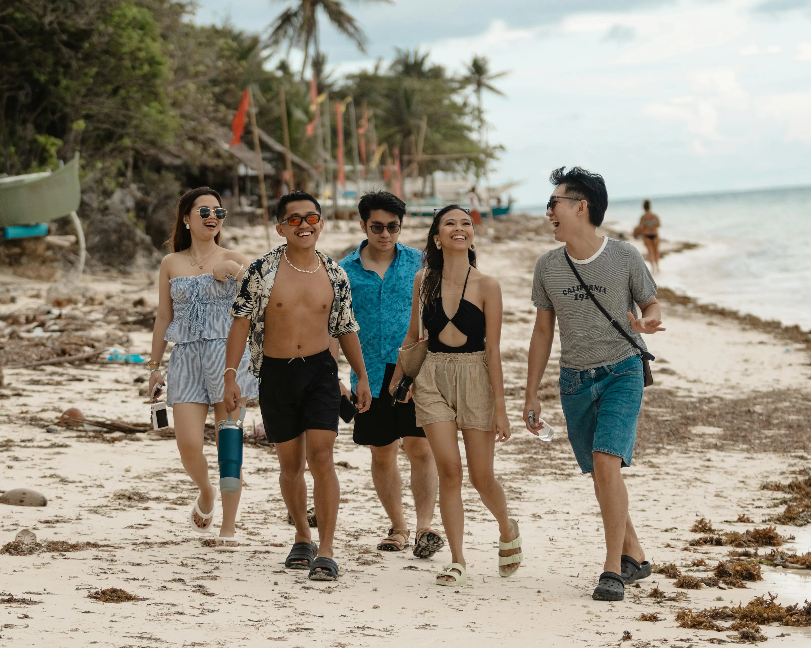 Five friends laughing together as they walk along a tropical beach